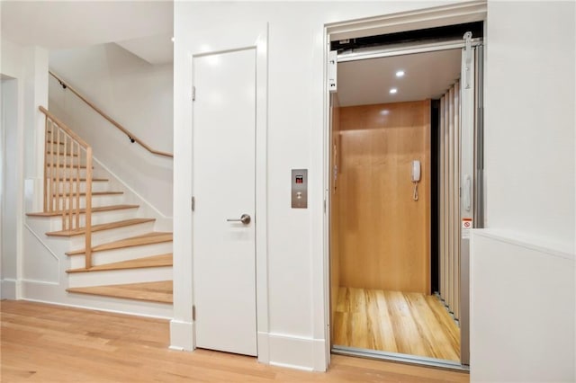 staircase featuring elevator, wood finished floors, and recessed lighting