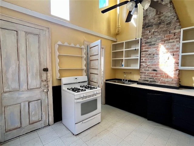 kitchen featuring a high ceiling, white gas range oven, ceiling fan, and sink