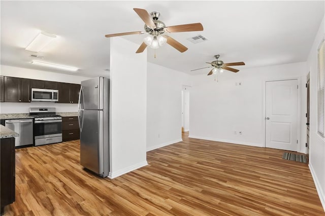 kitchen featuring stainless steel appliances, light stone countertops, dark brown cabinets, and light wood-type flooring