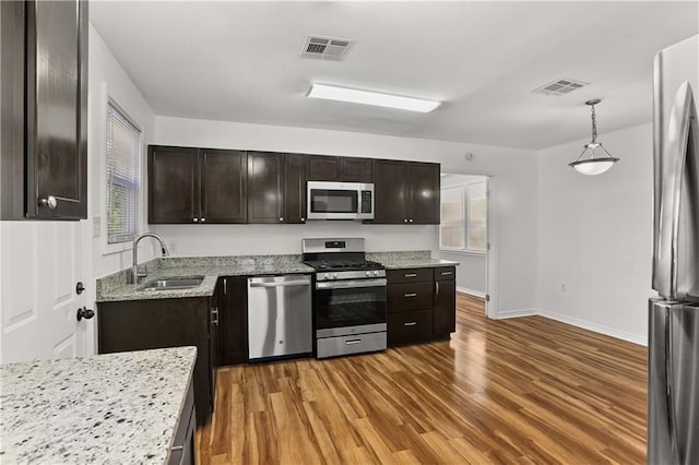 kitchen with appliances with stainless steel finishes, pendant lighting, wood-type flooring, sink, and dark brown cabinetry