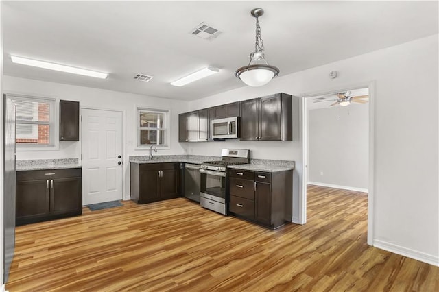 kitchen featuring sink, decorative light fixtures, dark brown cabinets, light hardwood / wood-style flooring, and appliances with stainless steel finishes