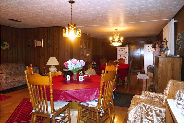 dining area with hardwood / wood-style floors, a chandelier, and wood walls