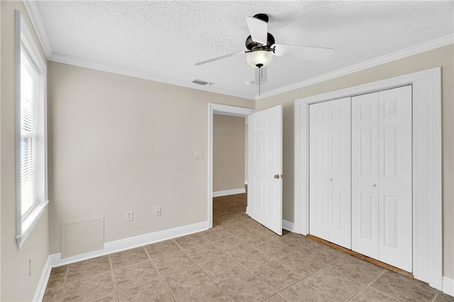 unfurnished bedroom with ceiling fan, a textured ceiling, light tile patterned floors, crown molding, and a closet