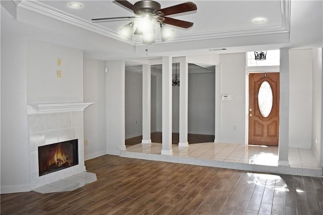 foyer with hardwood / wood-style floors, a tiled fireplace, ceiling fan, a raised ceiling, and crown molding