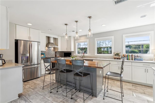 kitchen with stainless steel appliances, wall chimney range hood, white cabinets, and plenty of natural light