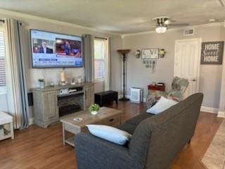 living room with ornamental molding, dark wood-type flooring, and ceiling fan