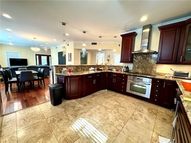 kitchen featuring oven, wall chimney exhaust hood, pendant lighting, crown molding, and light hardwood / wood-style flooring