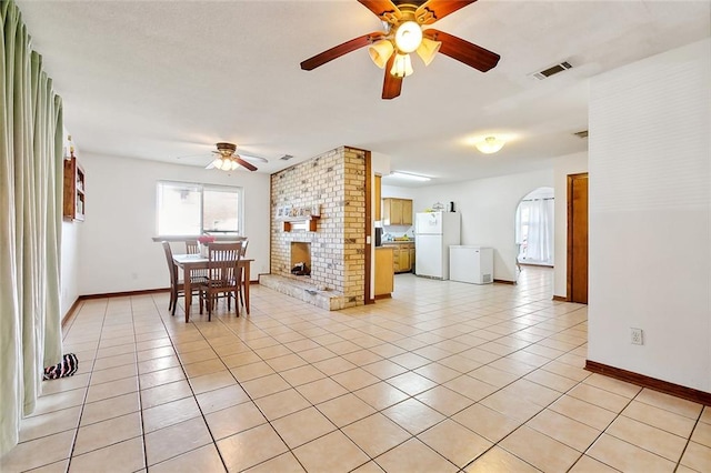 interior space with a brick fireplace, ceiling fan, and light tile patterned floors