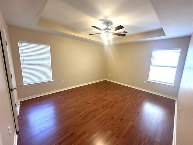 spare room with dark hardwood / wood-style flooring, a tray ceiling, and ceiling fan