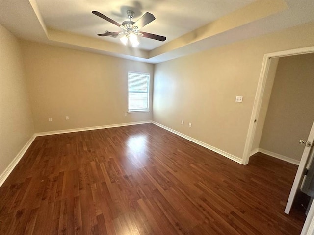 empty room featuring dark hardwood / wood-style flooring, a tray ceiling, and ceiling fan