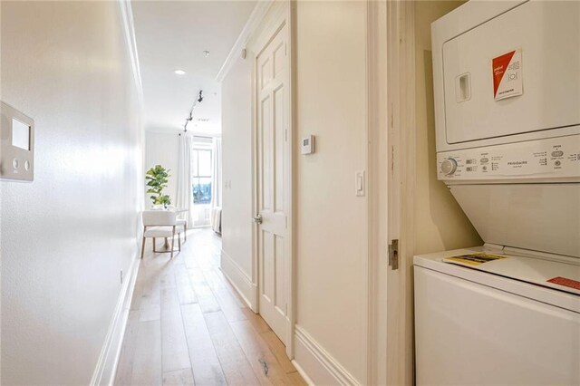 laundry area with ornamental molding, stacked washer and clothes dryer, and light wood-type flooring