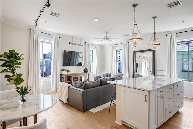 kitchen featuring a kitchen island, white cabinetry, light stone countertops, light wood-type flooring, and pendant lighting