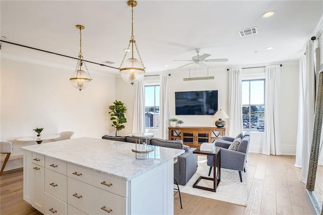 kitchen featuring a wealth of natural light, a kitchen island, white cabinets, and decorative light fixtures