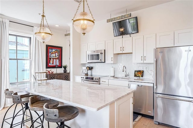 kitchen featuring hanging light fixtures, a center island, white cabinetry, appliances with stainless steel finishes, and light hardwood / wood-style floors