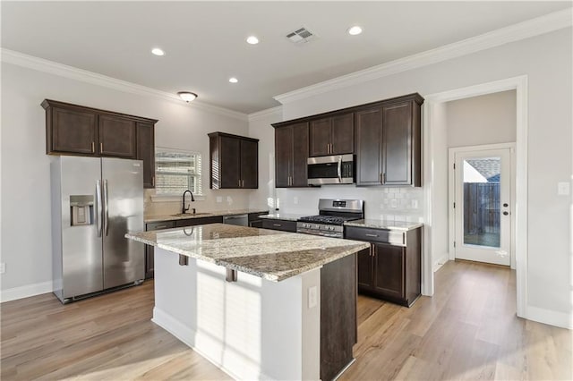 kitchen with sink, light hardwood / wood-style floors, appliances with stainless steel finishes, a kitchen island, and light stone counters