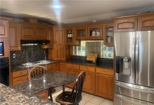 kitchen featuring decorative backsplash, dark stone countertops, stainless steel appliances, and light tile patterned floors