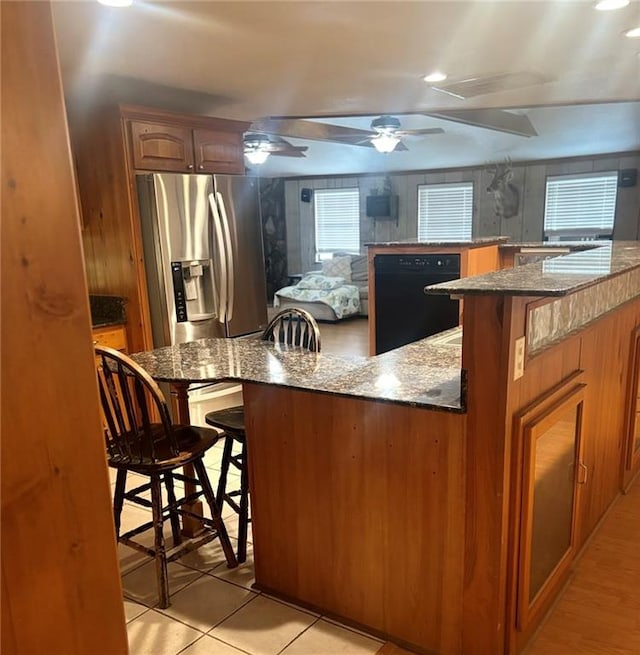 kitchen featuring dishwasher, a kitchen breakfast bar, kitchen peninsula, dark stone countertops, and stainless steel fridge