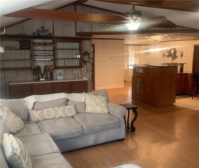 living room featuring ceiling fan, lofted ceiling with beams, light wood-type flooring, and wooden walls