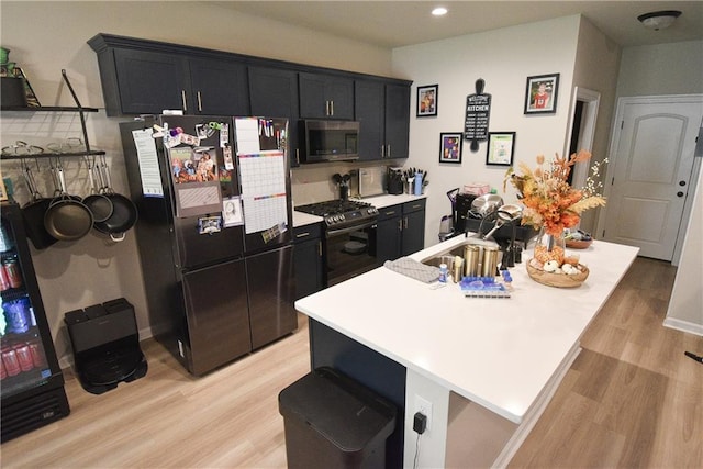 kitchen with light hardwood / wood-style floors, stainless steel appliances, sink, and a center island with sink