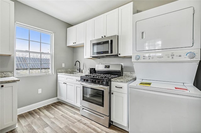 2437 Dumaine St, New Orleans, LA 70119 - kitchen featuring stainless steel appliances, stacked washer / dryer, light wood-style floors, white cabinetry, and light stone countertops