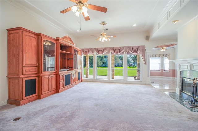 unfurnished living room with crown molding, a premium fireplace, light colored carpet, and ceiling fan