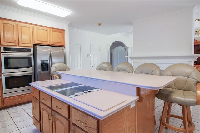 kitchen featuring a breakfast bar area, stainless steel appliances, crown molding, light tile patterned flooring, and a center island