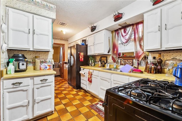 kitchen with a textured ceiling, white cabinets, black appliances, and sink