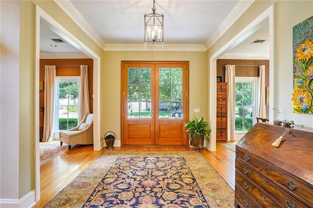 entryway with crown molding, a chandelier, light hardwood / wood-style floors, and french doors