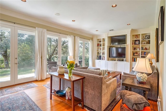 living room featuring crown molding, built in shelves, light hardwood / wood-style floors, and french doors