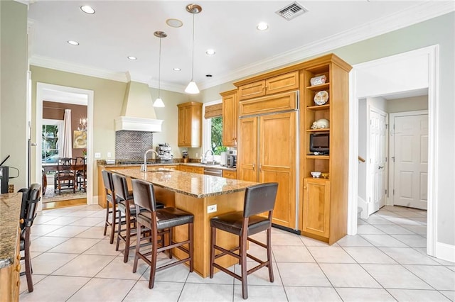 kitchen with custom exhaust hood, crown molding, an island with sink, and decorative light fixtures