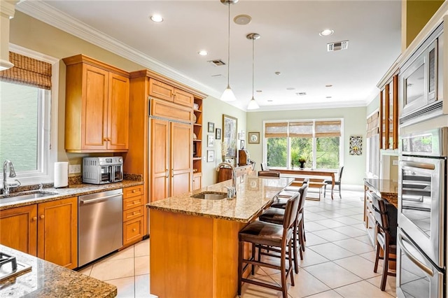 kitchen with hanging light fixtures, built in appliances, sink, and a center island with sink