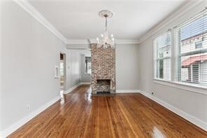 unfurnished living room with a large fireplace, hardwood / wood-style floors, crown molding, and a chandelier