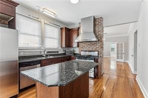 kitchen with a kitchen island, dark stone countertops, light hardwood / wood-style floors, wall chimney exhaust hood, and stainless steel appliances