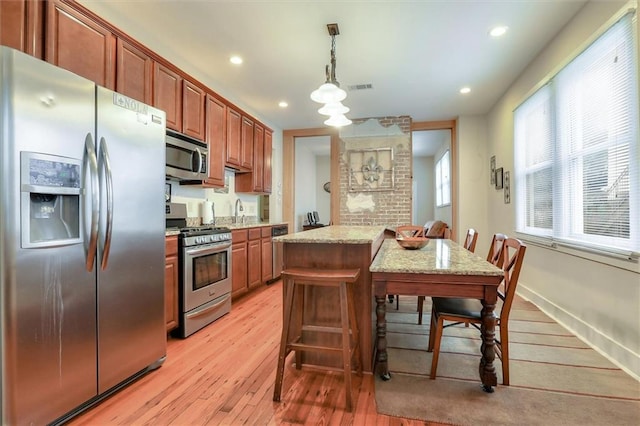 kitchen with appliances with stainless steel finishes, light wood-type flooring, a kitchen island, pendant lighting, and a breakfast bar area