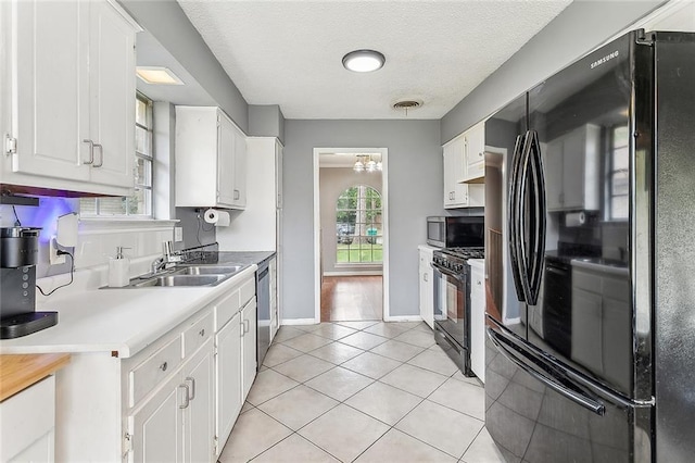 kitchen featuring a textured ceiling, sink, black appliances, light tile patterned floors, and white cabinetry