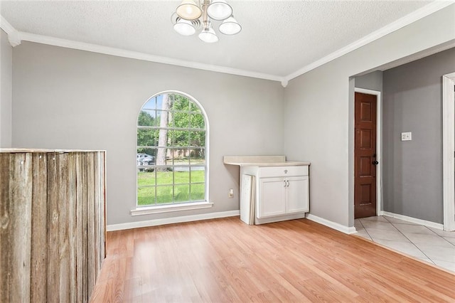 unfurnished dining area featuring crown molding, light hardwood / wood-style floors, a textured ceiling, and an inviting chandelier