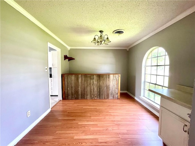 empty room featuring crown molding, light hardwood / wood-style floors, a textured ceiling, and an inviting chandelier