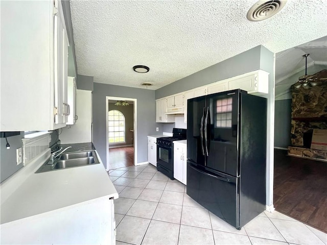 kitchen with a textured ceiling, sink, black appliances, light tile patterned floors, and white cabinets