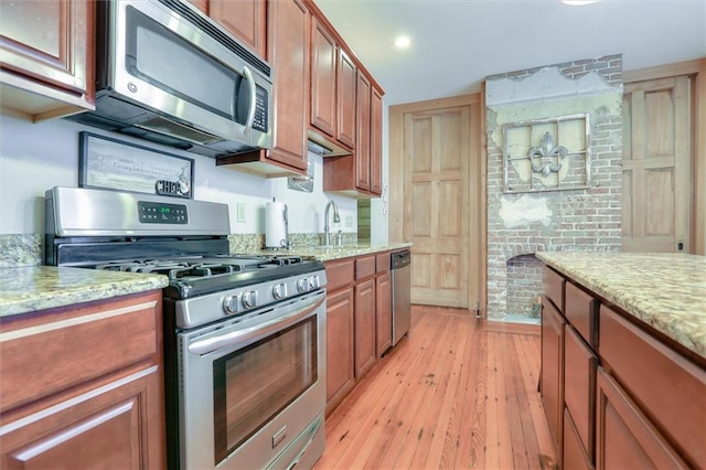 kitchen with appliances with stainless steel finishes, light stone counters, and light wood-type flooring