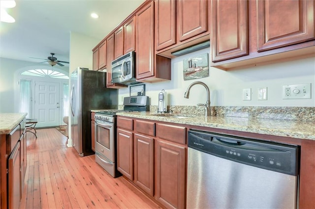 kitchen featuring ceiling fan, appliances with stainless steel finishes, sink, light hardwood / wood-style floors, and light stone counters