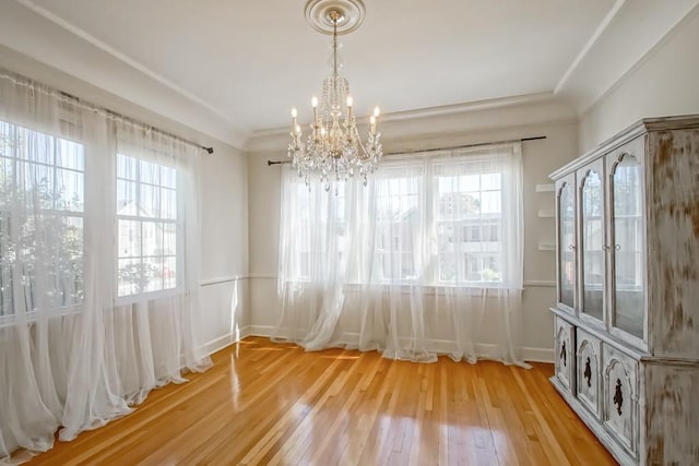 unfurnished dining area featuring a notable chandelier, ornamental molding, and light hardwood / wood-style flooring