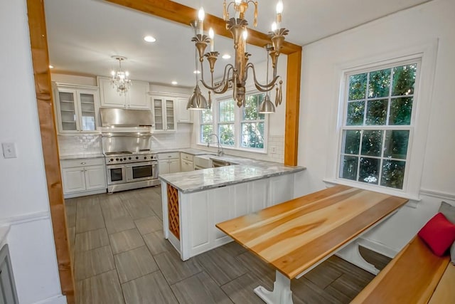 kitchen with kitchen peninsula, white cabinets, double oven range, and hanging light fixtures