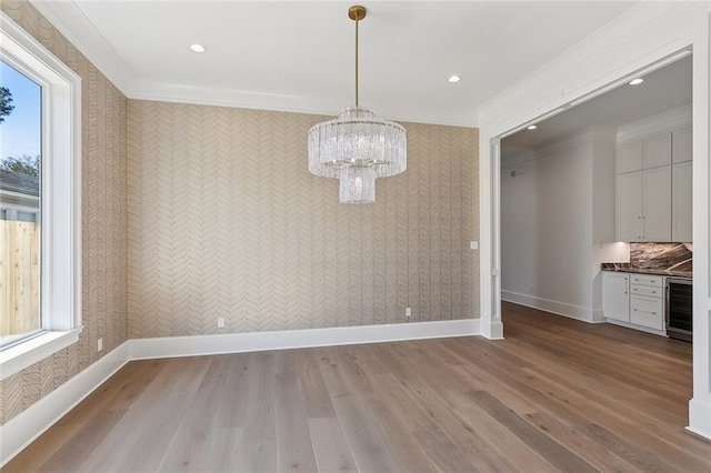 unfurnished dining area with wine cooler, an inviting chandelier, light hardwood / wood-style flooring, and crown molding