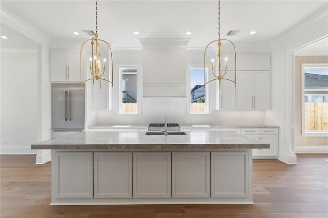 kitchen with white cabinetry, built in refrigerator, an island with sink, a chandelier, and light hardwood / wood-style floors