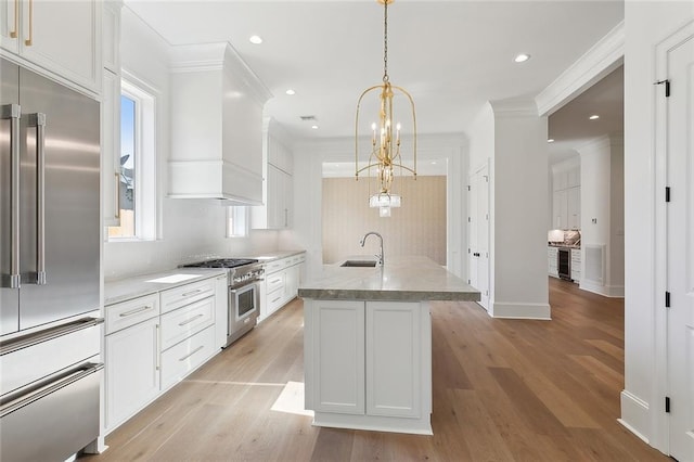 kitchen with pendant lighting, light hardwood / wood-style flooring, a kitchen island with sink, and high quality appliances