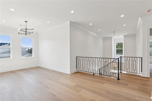 empty room featuring light wood-type flooring, ornamental molding, and a notable chandelier