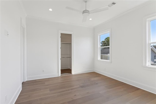 unfurnished bedroom with ceiling fan, wood-type flooring, a spacious closet, and ornamental molding