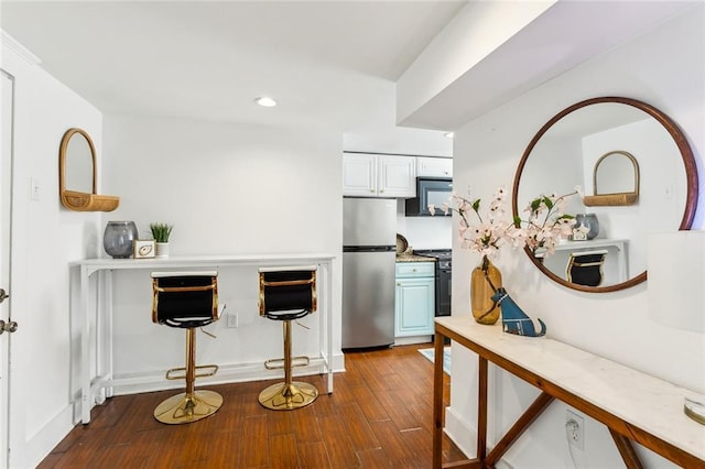 kitchen with stove, stainless steel fridge, white cabinetry, and dark hardwood / wood-style floors