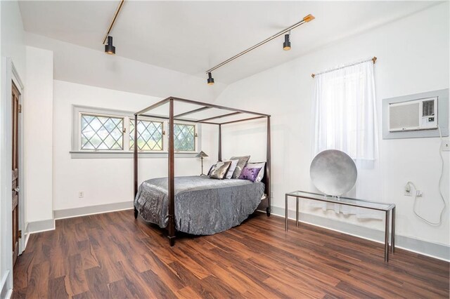 bedroom with dark hardwood / wood-style floors, a wall mounted AC, and track lighting