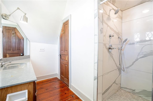 bathroom featuring a tile shower, vanity, wood-type flooring, and vaulted ceiling